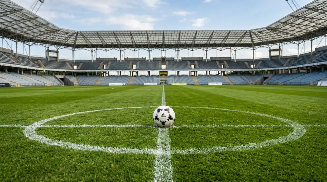 Bola de futebol no centro de um relvado verde com marcacoes brancas num estadio vazio