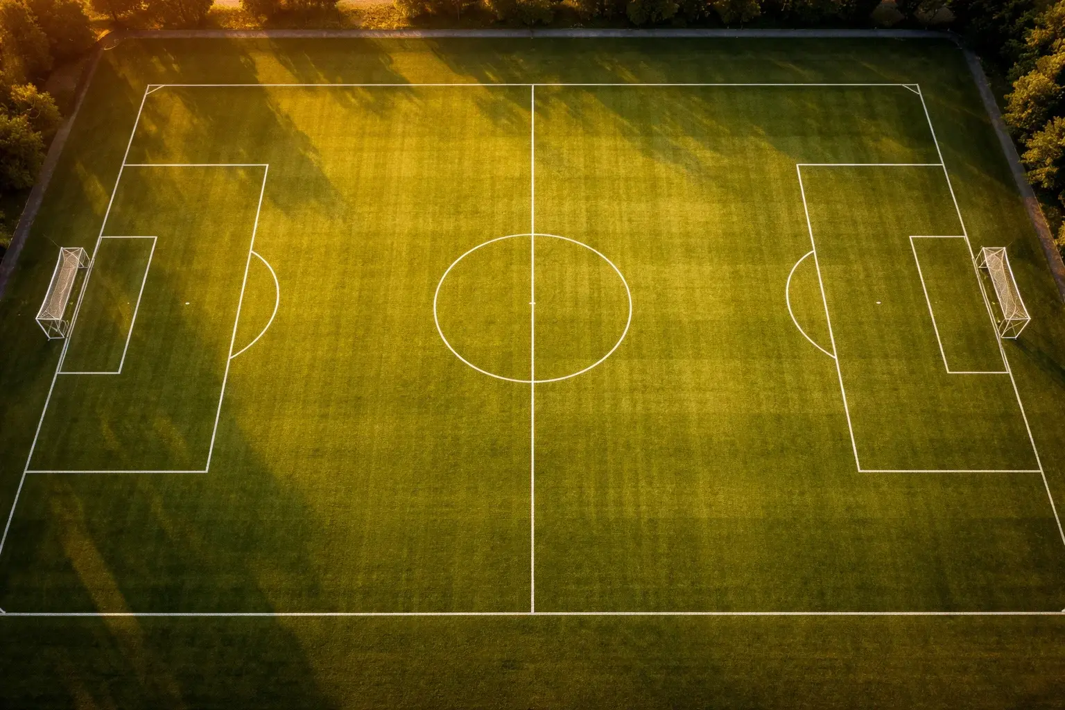 Campo de futebol visto de cima com linhas de marcacao bem visiveis ao por do sol
